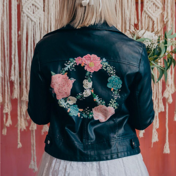 Girl wears black leather jacket with floral peace symbol painted on the back.