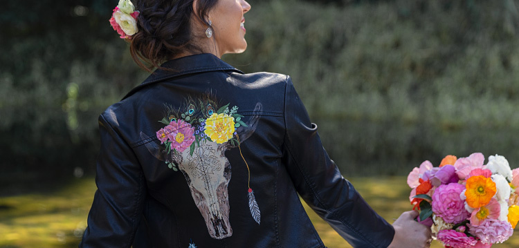 Girl holds bouquet of flowers and wears black leather jacket with cow skull and florals.