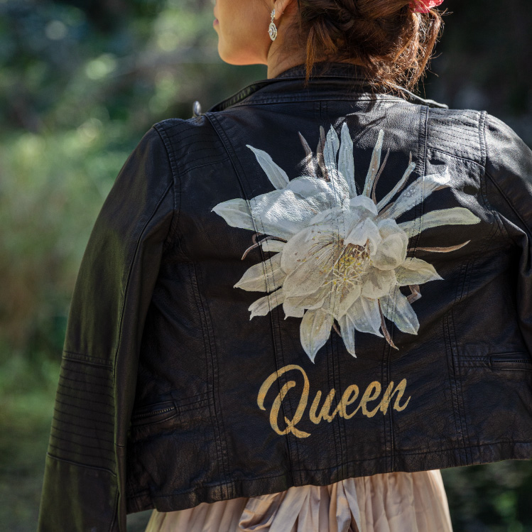 Girl wears black leather jacket with big white flower and words 'Queen' painted on the back.,