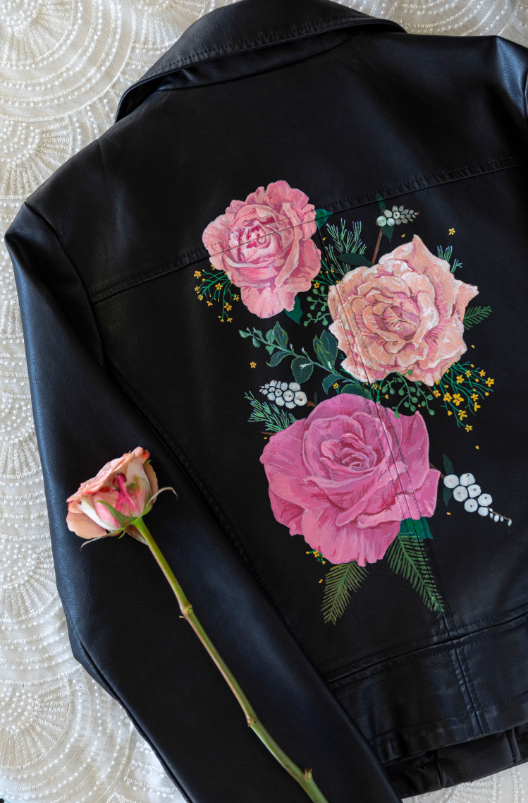 The back of a black leather jacket with rose florals painted on.